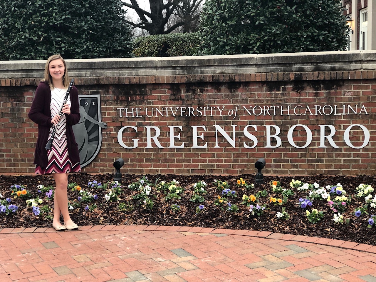 Student in front of UNC-G Sign Student holding musical instrument in front of the UNC-Greensboro sign.